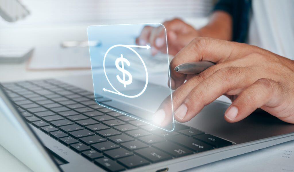 Close-up of hands using a laptop with a dollar sign graphic above the keyboard