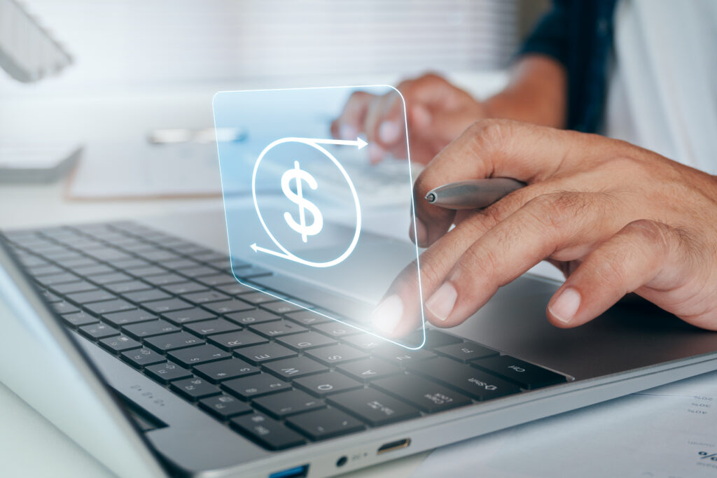 Close-up of hands using a laptop with a dollar sign graphic above the keyboard