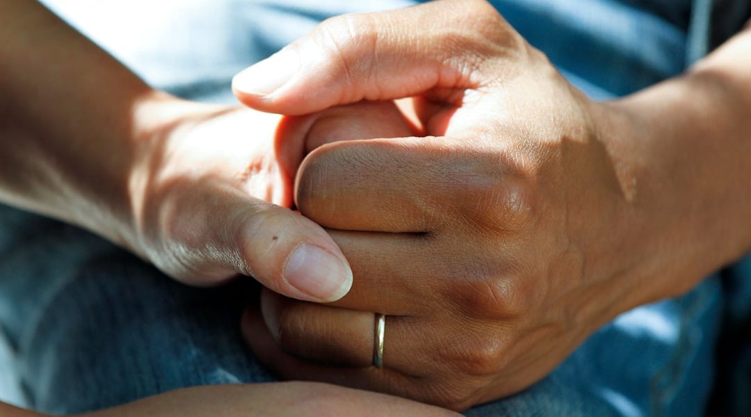 Close-up of two hands clasped together, suggesting support and comfort.