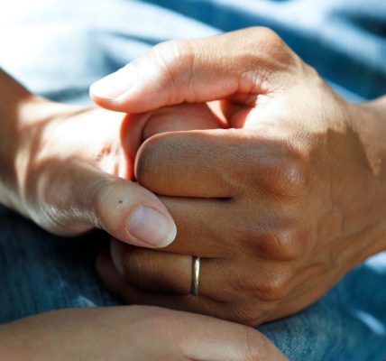 Close-up of two hands clasped together, suggesting support and comfort.
