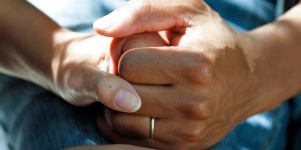 Close-up of two hands clasped together, suggesting support and comfort.